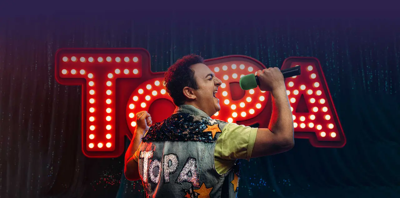Diego Topa cantando con micrófono frente al cartel luminoso de TOPA
